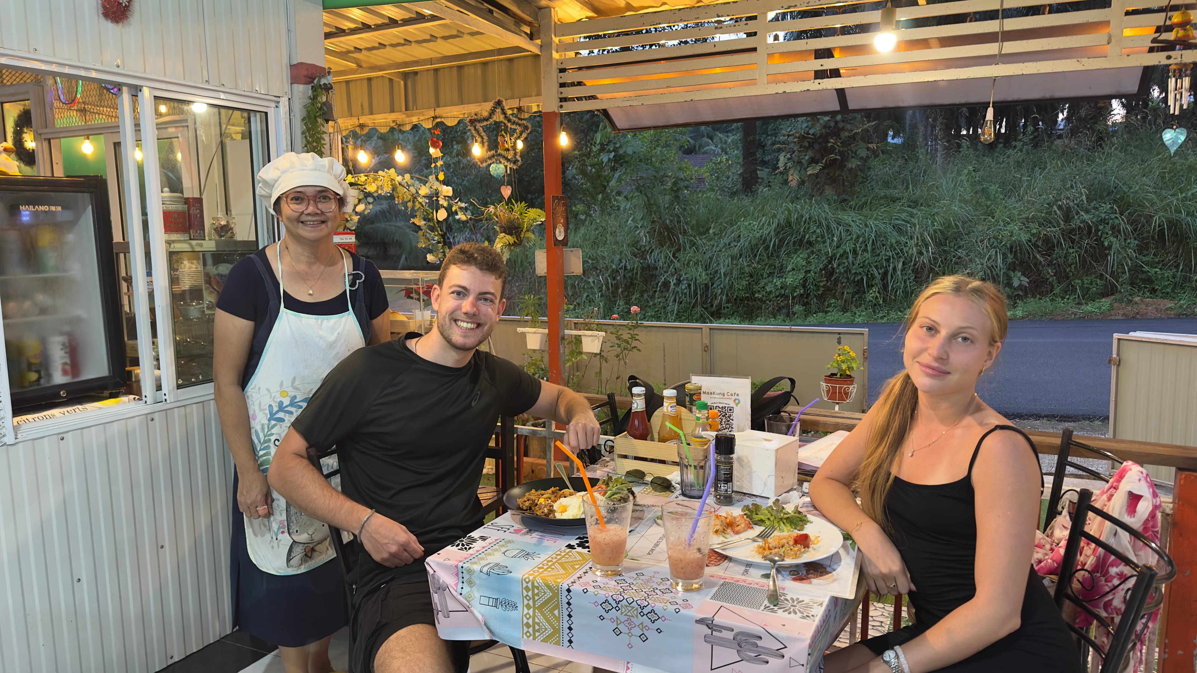 Owner serving guests dinner under warm fairy lights at MaeKung Cafe Krabi