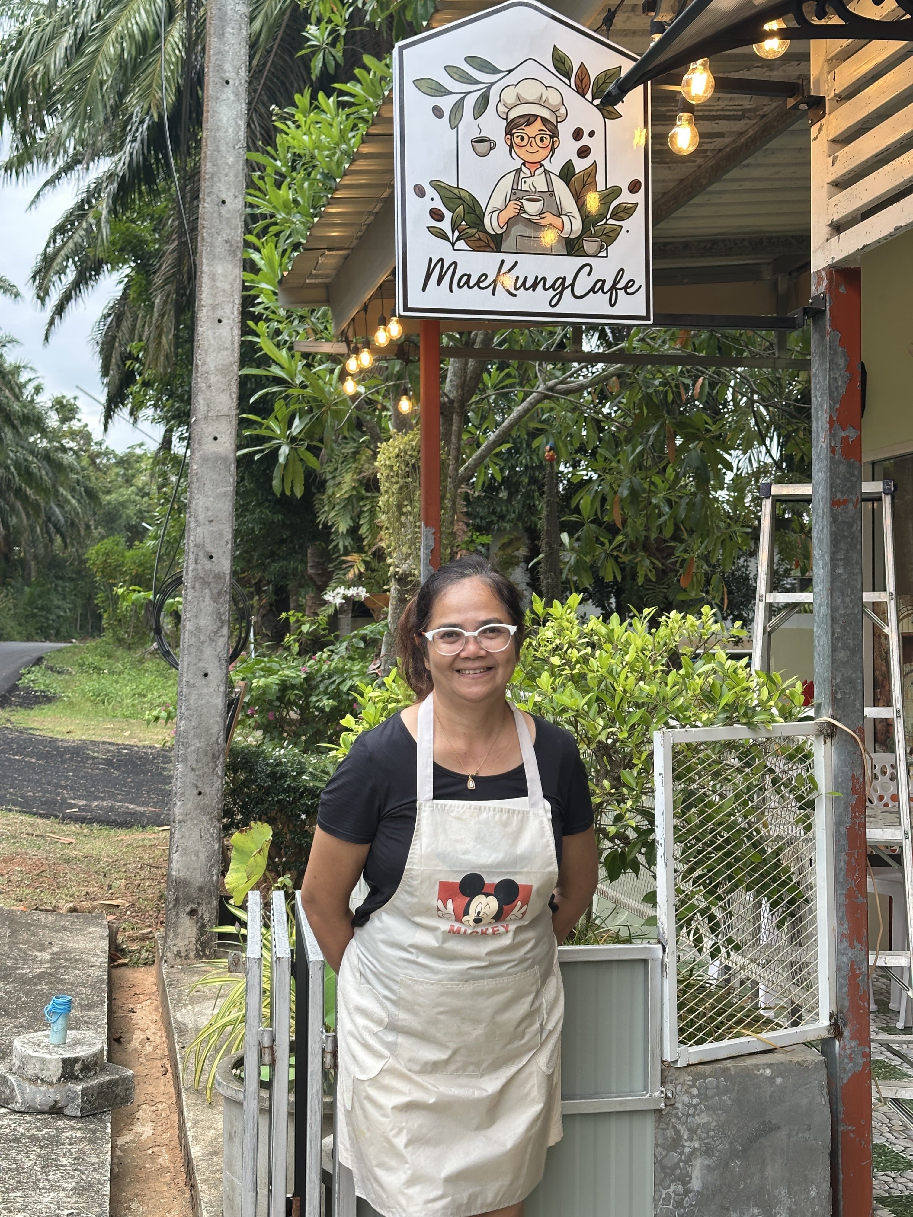 Owner of MaeKung Cafe standing in front of the cafe sign, Krabi Town